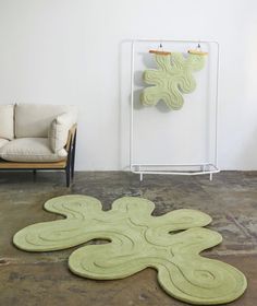 a green rug on the floor in front of a chair and wall with an art piece