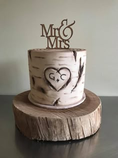 a wedding cake with the initials mr and mrs painted on it is sitting on top of a tree stump