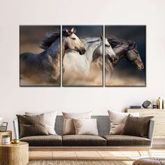 three horses running together in the wild on a wall above a couch and coffee table