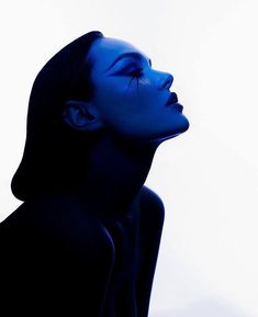 a woman with blue makeup and black hair is looking off into the distance while standing in front of a white background