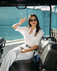 a woman sitting in the back of a truck with her hand up and wearing sunglasses