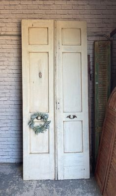 two white doors with wreaths on them in front of a brick wall and door