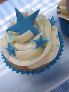 cupcakes with white frosting and blue stars are on a tableclothed surface