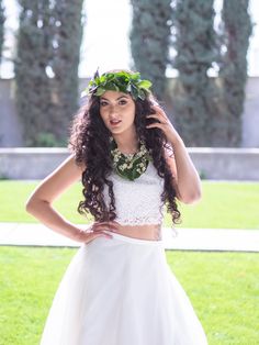 a woman in a white dress and wreath on her head is posing for the camera