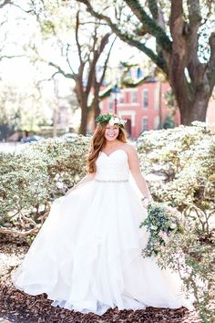 a woman in a white wedding dress is standing under some trees and holding a bouquet