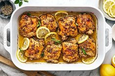 chicken with lemons and herbs in a white casserole on a marble table