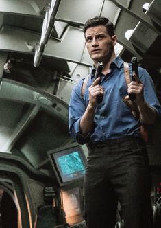 a man in a blue shirt and black pants holding a microphone while standing next to a space station