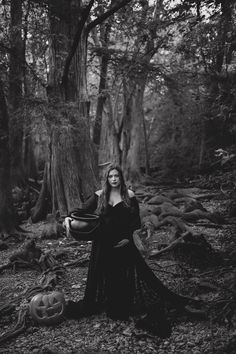 a woman in a black dress standing in the woods with her hands on her hips