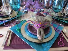 the table is set with purple and blue plates, napkins, silverware, and beads