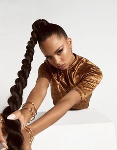 a woman sitting on top of a white box holding her hair in one hand and looking at the camera