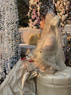 a woman in a wedding dress sitting on a white bench next to a flower covered wall