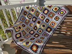 a crocheted granny blanket sitting on top of a wooden bench next to flowers