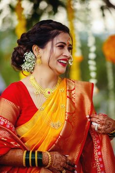 a woman in an orange and yellow sari smiles at the camera while wearing gold jewelry