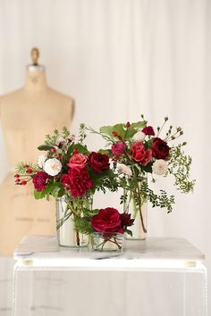 two vases filled with red and white flowers on top of a table next to a mannequin