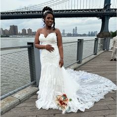 a woman in a white wedding dress standing on a pier next to the brooklyn bridge