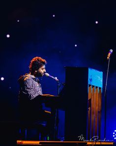 a man that is sitting at a piano in front of a microphone and some lights