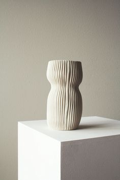 a white vase sitting on top of a block of concrete in front of a wall