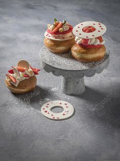 three donuts with strawberries and whipped cream on top are sitting on a cake stand