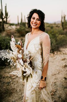 a woman in a white dress holding a bouquet of wildflowers and cactus plants