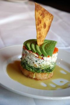 a white plate topped with an appetizer covered in guacamole and tortilla chips