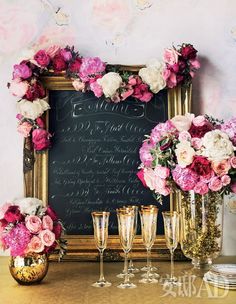 a table topped with lots of pink flowers next to a chalkboard covered in writing