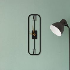 a black clock mounted to the side of a green wall next to a floor lamp