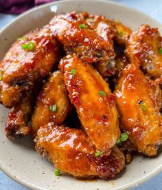 a white bowl filled with chicken wings covered in sauce and garnished with green onions