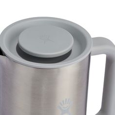 a stainless steel coffee pot with a lid and handle on the side, sitting next to a cup holder