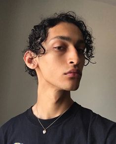 a young man with curly hair wearing a black t - shirt and looking off into the distance