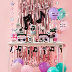 a party table with balloons, streamers, and music notes on it in front of a pink wall