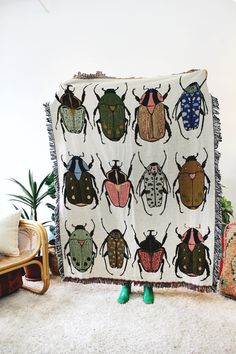 a blanket with many different bugs on it in front of a chair and potted plant