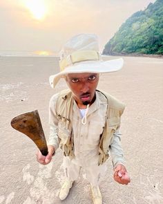 a young man wearing a white hat and holding an ax in his hand on the beach