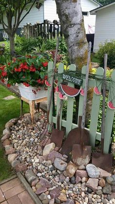 a garden with flowers and gardening tools in the ground next to a fence that says welcome