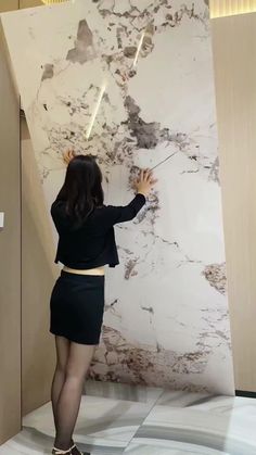 a woman in black shirt and skirt standing next to marble wall with lights on it