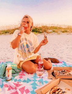 a woman sitting on the beach eating pizza and drinking wine