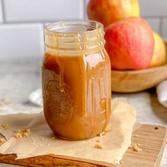 a jar filled with peanut butter sitting on top of a cutting board next to apples