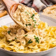 a wooden spoon scooping some food out of a white bowl on top of pasta