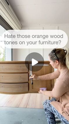 a woman sitting on top of a wooden floor next to a dresser and holding a paintbrush