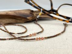 Shiny and bohemian eyeglass necklace chain in copper and gold tones, made with Preciosa Czech crystal seed beads and tiny Sunstone gemstone beads.    Paired with delicate copper plated Japanese Miyuki crystal seed beads and gold touches of the Sunstone gems, this handmade eyeglass chain will definitely create a unique look. Sunstone is linked to luck and good fortune. It instills good nature, heightens intuition and allows the real self to shine through happily. It alleviates stress and increase Artisan Adjustable Glass Beads, Adjustable Brown Beaded Necklace, Adjustable Brown Beaded Round Necklace, Adjustable Brown Round Beaded Necklace, Adjustable Round Brown Beaded Necklace, Adjustable Glass Necklaces With Tiny Beads, Adjustable Glass Necklace With Tiny Beads, Adjustable Glass Beaded Necklace With Gemstone Beads, Adjustable Glass Gemstone Beaded Necklaces