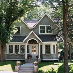 a gray and white house in the middle of some trees with potted plants on the front porch