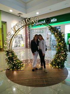 two women standing in front of a christmas display with lights on the trees and decorations