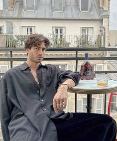 a man sitting at a table on top of a balcony next to a bottle of alcohol