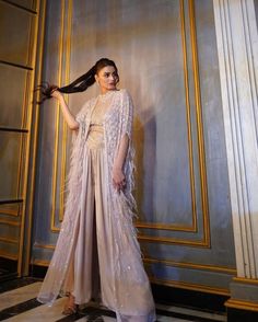 a woman standing in front of a wall wearing a long dress with feathers on it