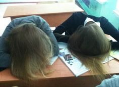 two women sitting at desks with books and papers in front of their heads,