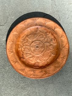 an orange plate sitting on top of a cement floor next to a black bowl with a flower design