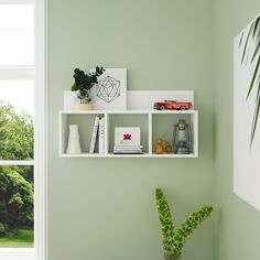 a white shelf with books and plants on it next to a window in a green room