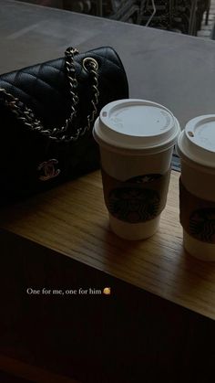 two cups of coffee sitting on top of a wooden table next to a handbag