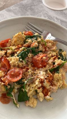 a white plate topped with eggs, tomatoes and spinach next to a cup of coffee