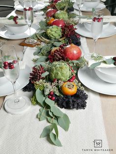 a long table is set with white plates and silverware for an elegant holiday dinner