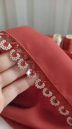 a woman's hand holding onto a red satin material with beading on it